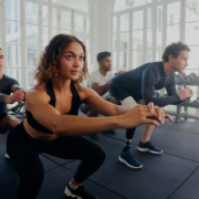 Group of focused multiracial young adults in sports clothing doing squats at the gym